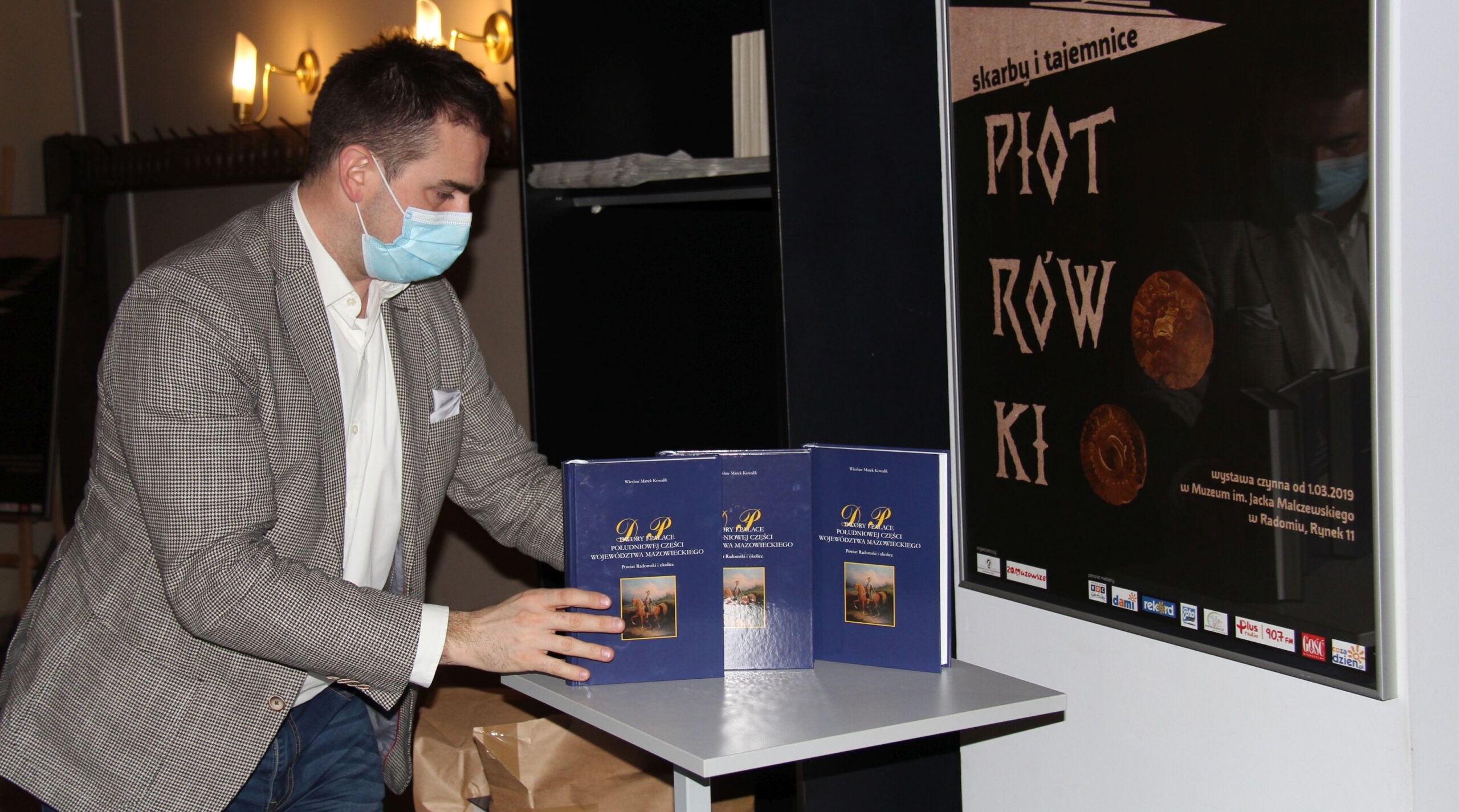 aIMG_3618 pracownikiem PIK wykłada na stole egzemplarze książki do sprzedaży, promocja książki M. Kowalika "Dwory i pałace"