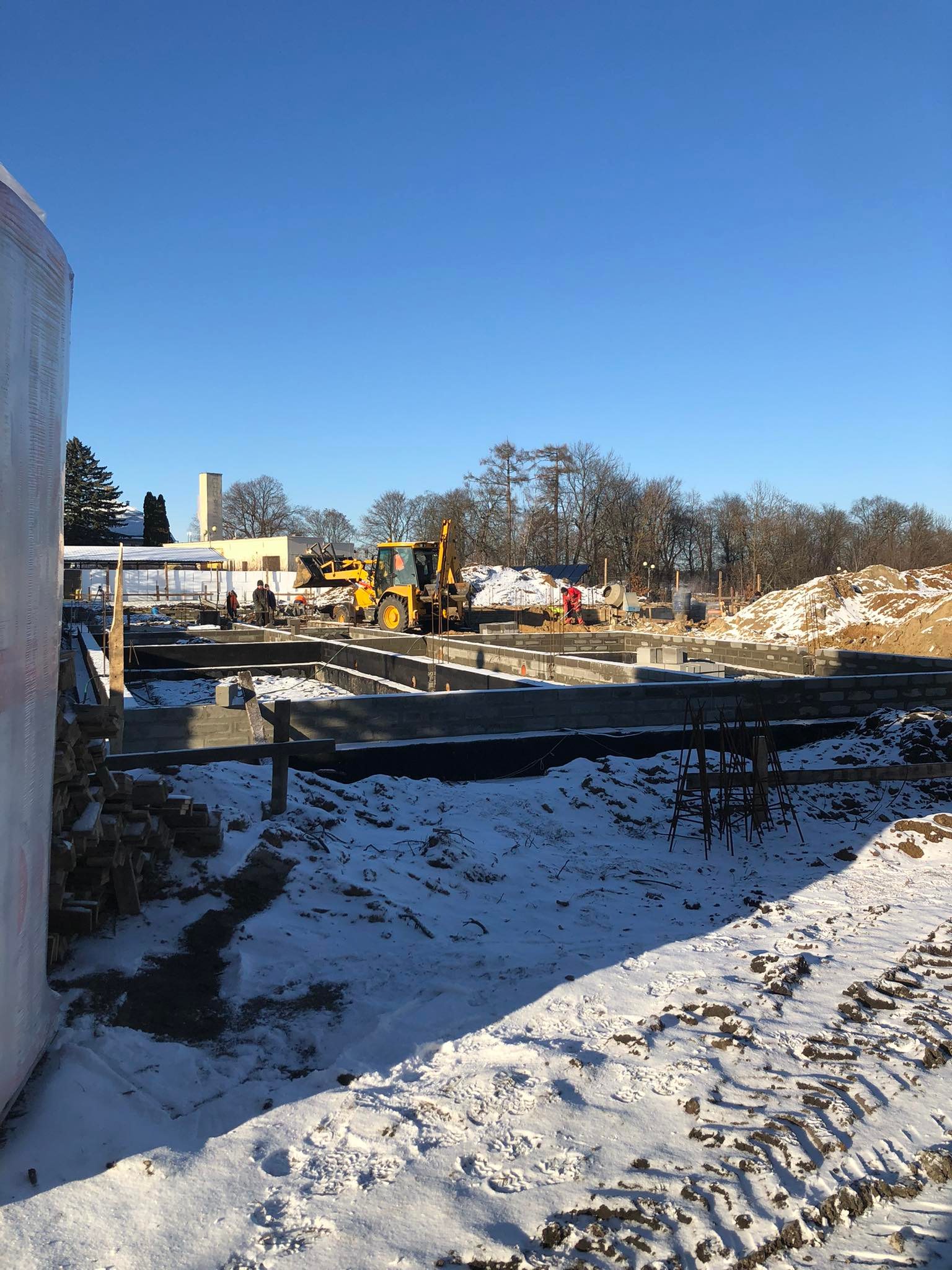 263773176_454520926322102_8691922537544685401_n Plac budowy pokryty lekkim śniegiem. Widać fundamenty, w tle pracuje koparka.