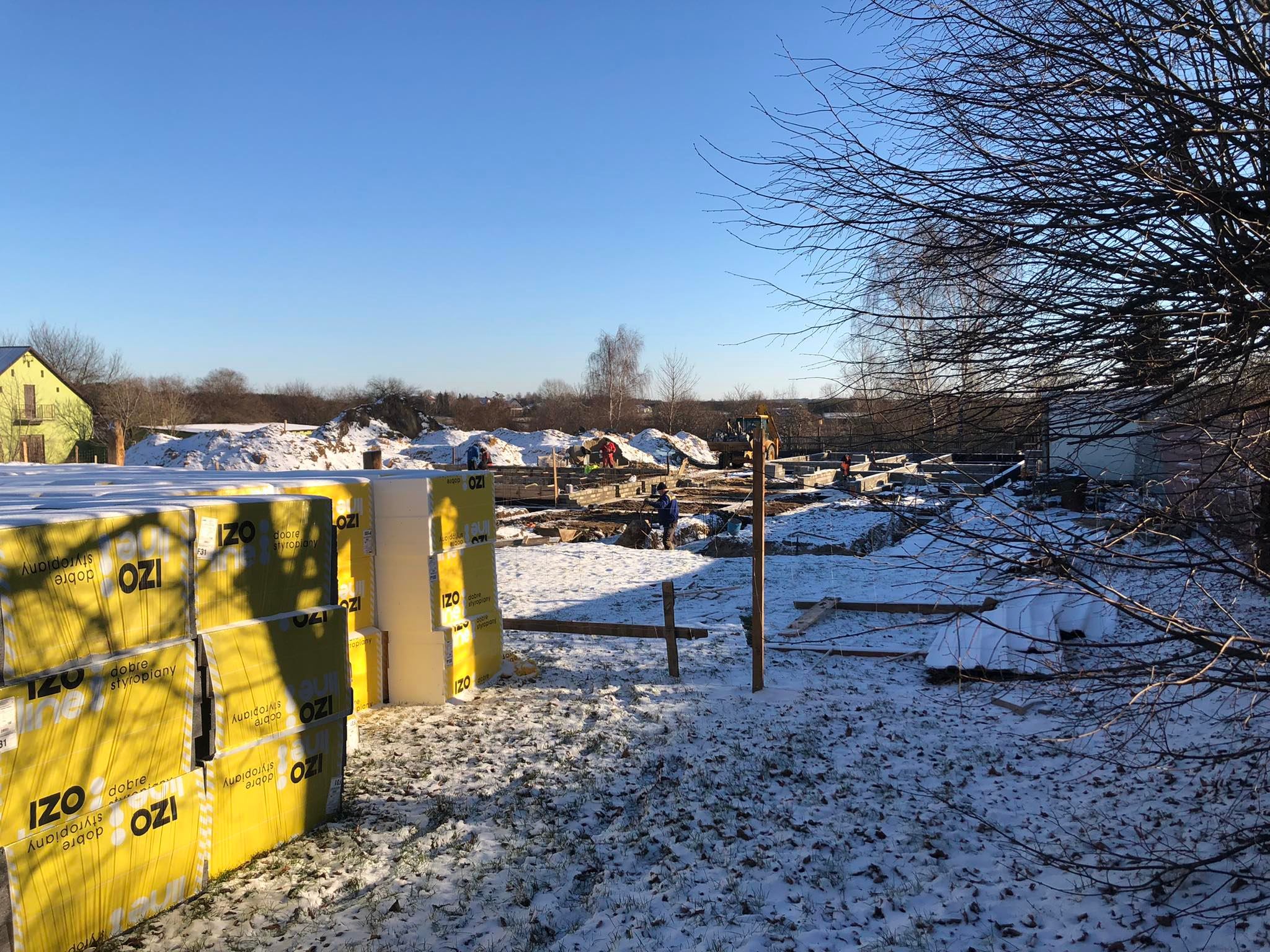 268035135_644497403234322_2504551579790186994_n Plac budowy pokryty lekkim śniegiem. Na pierwszym planie fundamenty i materiały budowlane.