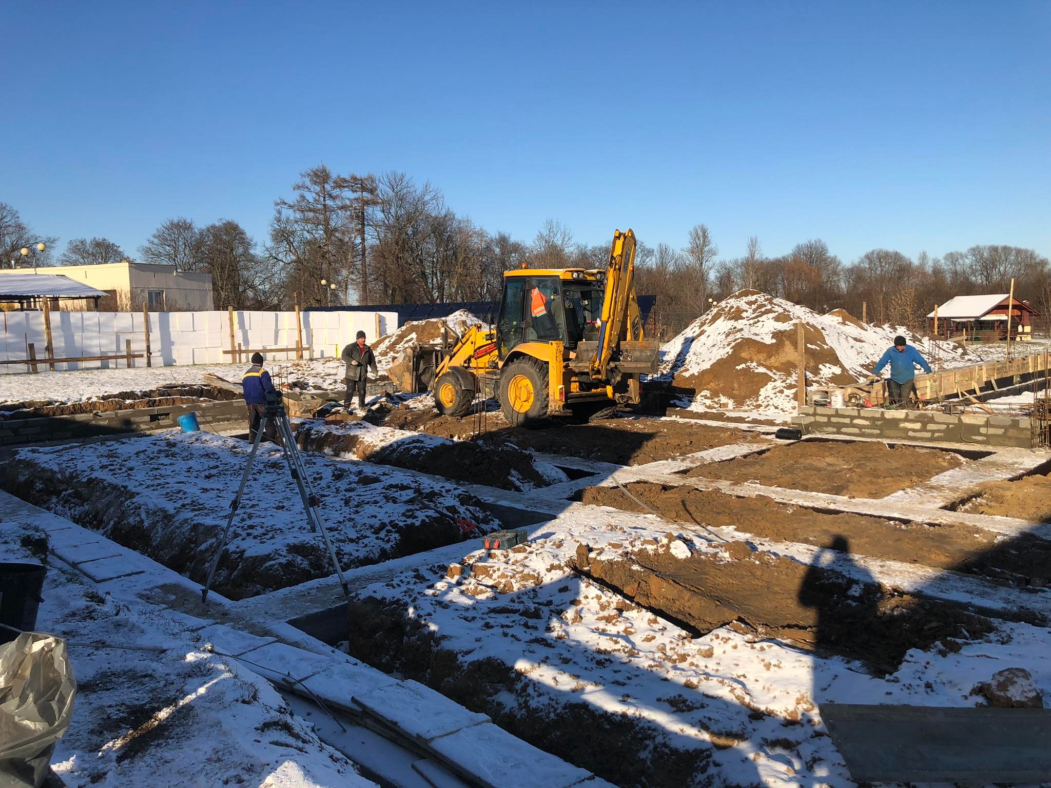 269102600_496692911667933_3152970581359771261_n Plac budowy pokryty lekkim śniegiem. Robotnicy wykonują prace przy fundamentach. W tle koparka.